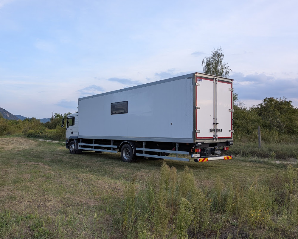 A box-truck build parked on a dirt track — a plain white truck from the outside