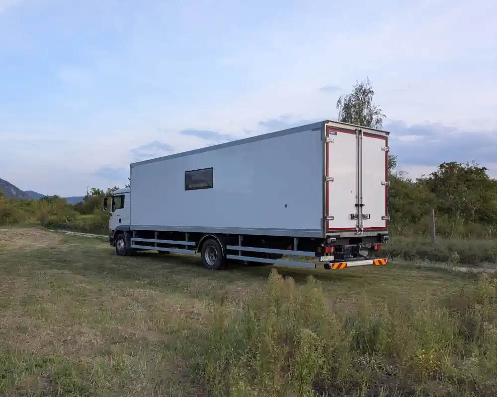 A box-truck build parked on a dirt track — a plain white truck from the outside